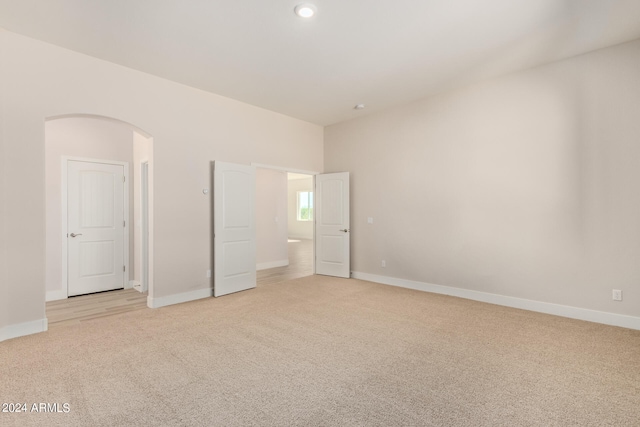 unfurnished bedroom featuring light carpet, baseboards, and arched walkways