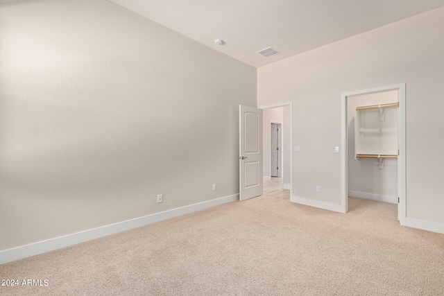 unfurnished bedroom featuring visible vents, baseboards, light colored carpet, a spacious closet, and a closet