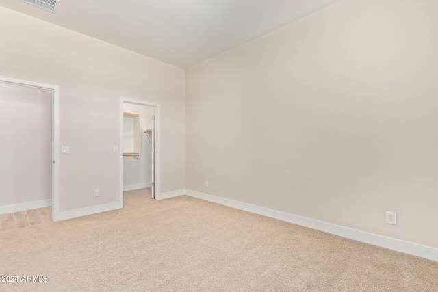 unfurnished bedroom featuring light carpet, baseboards, a spacious closet, and visible vents