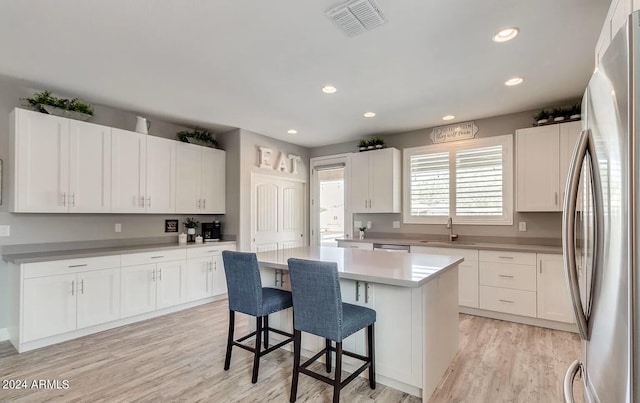 kitchen with light countertops, appliances with stainless steel finishes, white cabinetry, a kitchen island, and a sink