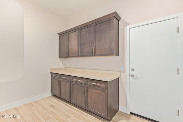 kitchen featuring wood finish floors, light countertops, dark brown cabinetry, and baseboards