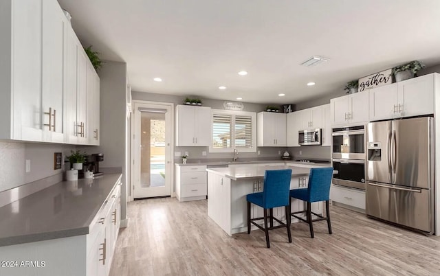 kitchen featuring stainless steel appliances, a sink, a kitchen island, white cabinetry, and a kitchen breakfast bar