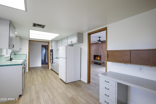 kitchen featuring sink, ceiling fan, a fireplace, white fridge, and white cabinetry