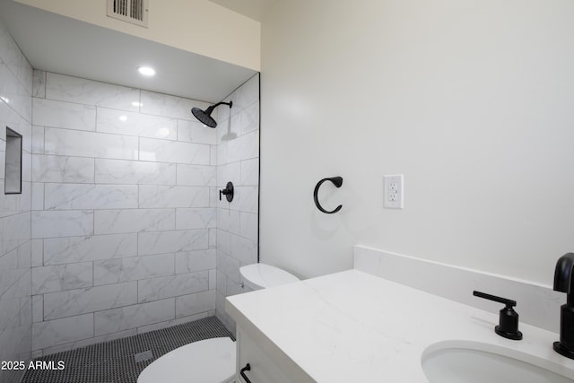 bathroom with tiled shower, vanity, and toilet