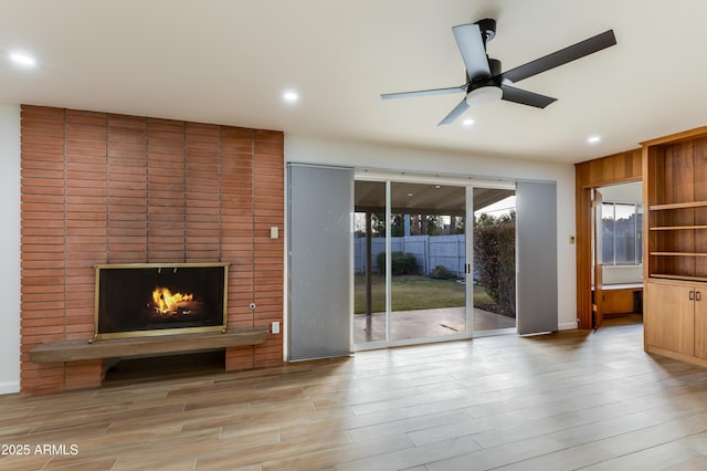 unfurnished living room featuring light hardwood / wood-style flooring, a brick fireplace, and ceiling fan