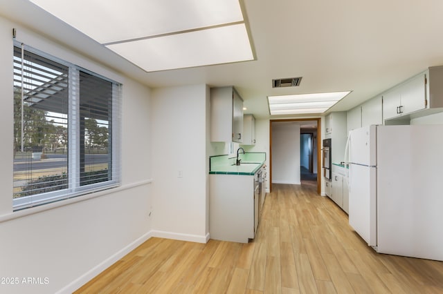 kitchen featuring white cabinets, white fridge, a wealth of natural light, and light hardwood / wood-style floors