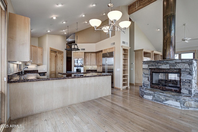 kitchen featuring built in shelves, built in appliances, light wood-type flooring, kitchen peninsula, and a fireplace