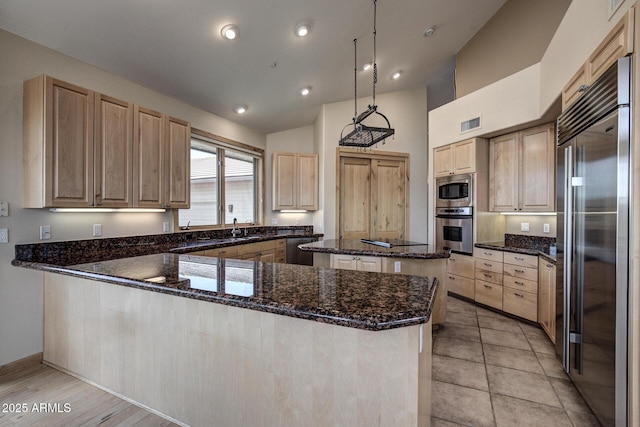 kitchen with a center island, dark stone countertops, appliances with stainless steel finishes, kitchen peninsula, and pendant lighting