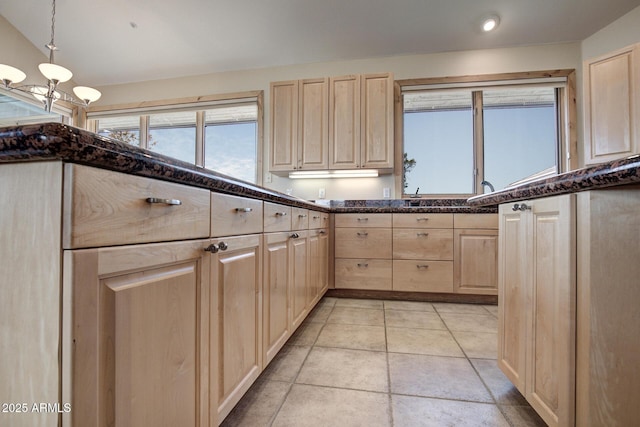 kitchen with lofted ceiling, light tile patterned floors, dark stone countertops, decorative light fixtures, and light brown cabinets