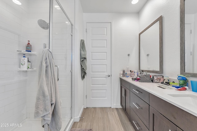 bathroom with a sink, double vanity, wood finish floors, and a shower stall