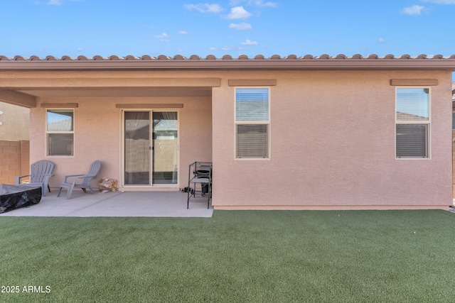 rear view of house featuring stucco siding, a lawn, and a patio