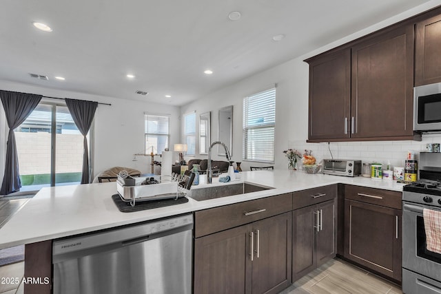 kitchen featuring appliances with stainless steel finishes, light countertops, a sink, and a peninsula