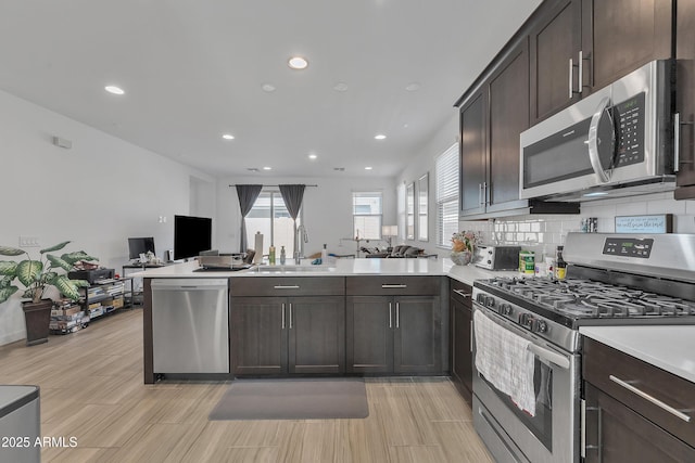 kitchen featuring stainless steel appliances, a peninsula, a sink, open floor plan, and light countertops