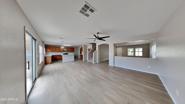 unfurnished living room featuring arched walkways, visible vents, a ceiling fan, light wood-type flooring, and baseboards