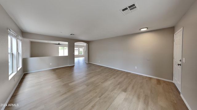 empty room featuring light wood-type flooring, baseboards, visible vents, and arched walkways