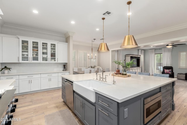 kitchen with gray cabinets, a sink, stainless steel appliances, open floor plan, and ornamental molding