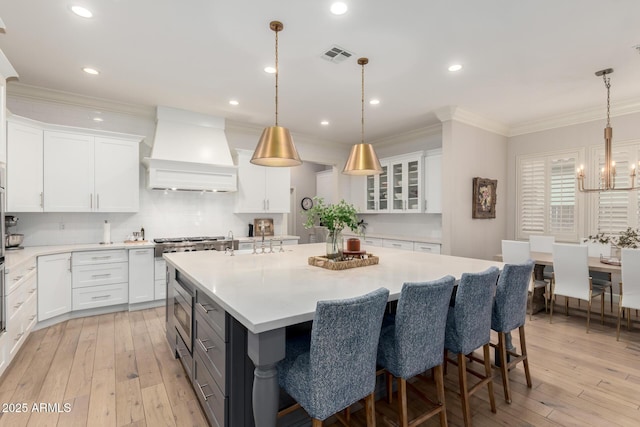 kitchen featuring premium range hood, a chandelier, white cabinetry, light countertops, and ornamental molding