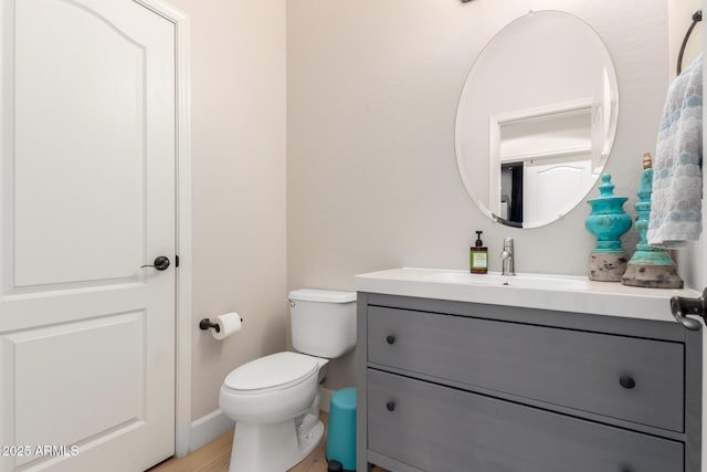 half bathroom with vanity, toilet, baseboards, and wood finished floors