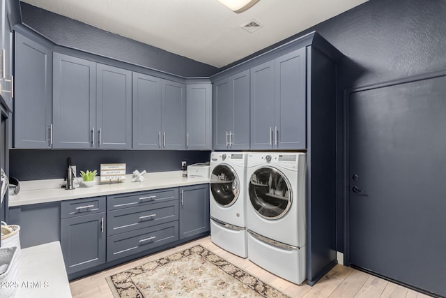 clothes washing area with cabinet space, washing machine and dryer, and light wood-style flooring