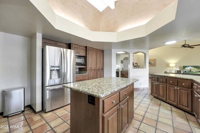 kitchen with a center island, stainless steel refrigerator with ice dispenser, black microwave, ceiling fan, and a tray ceiling