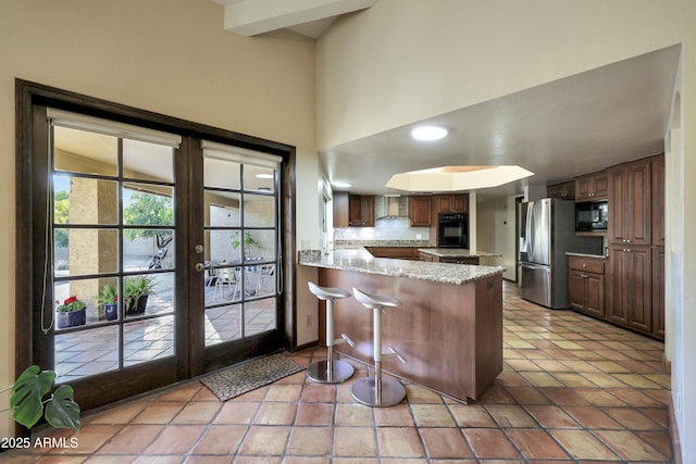 kitchen featuring black appliances, french doors, kitchen peninsula, light stone counters, and a breakfast bar area