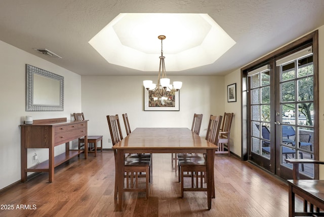 dining room featuring a textured ceiling, dark hardwood / wood-style flooring, a raised ceiling, and an inviting chandelier