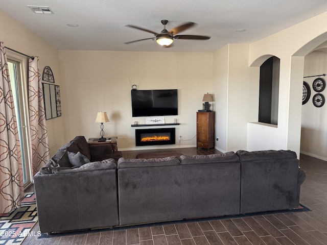 living area with visible vents, a glass covered fireplace, wood tiled floor, ceiling fan, and baseboards