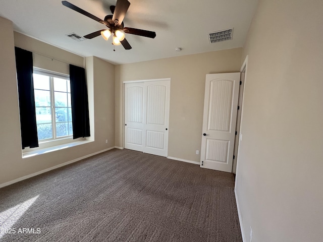 unfurnished bedroom with baseboards, visible vents, dark carpet, and a closet