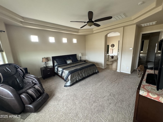 carpeted bedroom featuring arched walkways, a raised ceiling, visible vents, and baseboards