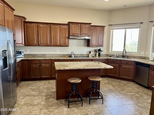 kitchen with stainless steel appliances, a sink, a kitchen island, under cabinet range hood, and a kitchen bar