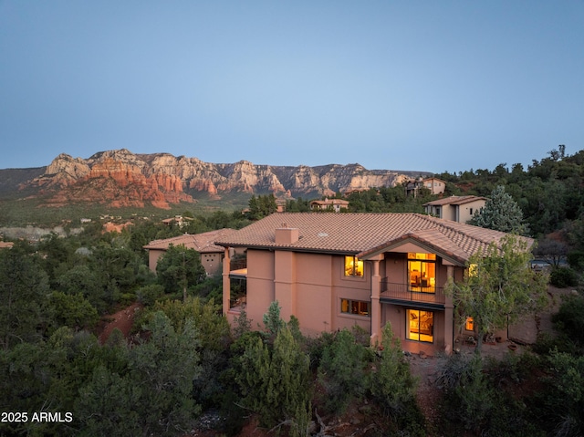 exterior space featuring a balcony, a chimney, a tiled roof, a mountain view, and stucco siding