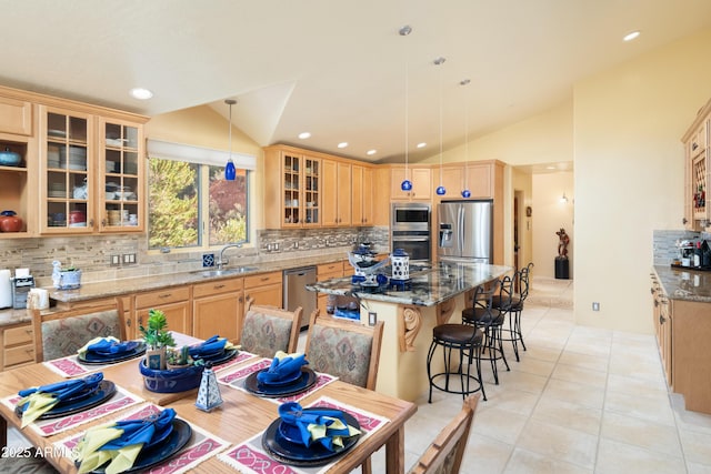 kitchen with light tile patterned floors, stainless steel appliances, lofted ceiling, a sink, and a kitchen island