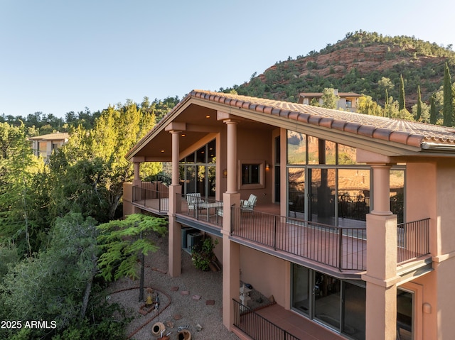 back of property with a balcony, stucco siding, a mountain view, and a tiled roof