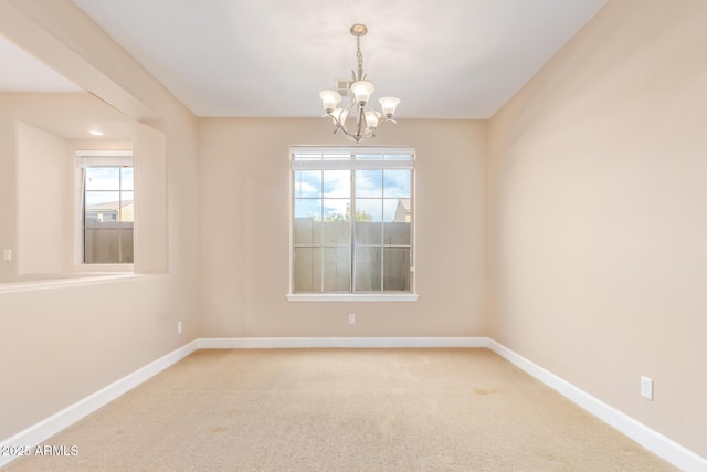 empty room featuring a chandelier, light carpet, and baseboards