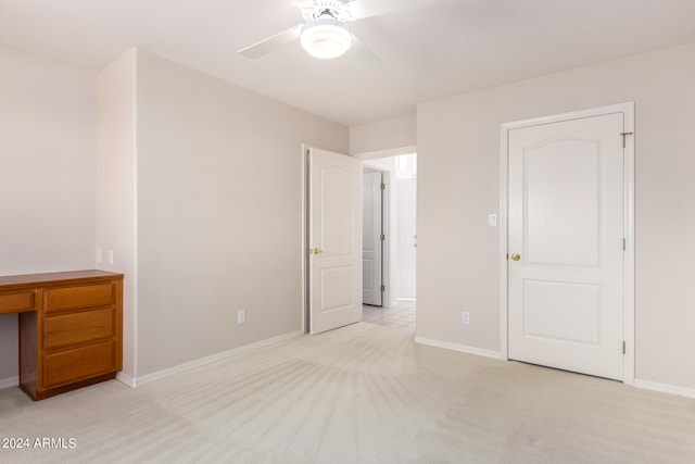 unfurnished bedroom with built in desk, light carpet, and ceiling fan