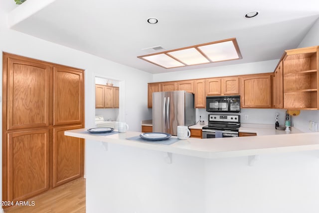 kitchen with a kitchen bar, appliances with stainless steel finishes, light hardwood / wood-style flooring, and kitchen peninsula