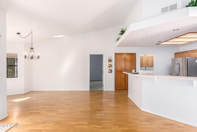 unfurnished living room featuring light hardwood / wood-style flooring, a notable chandelier, and high vaulted ceiling