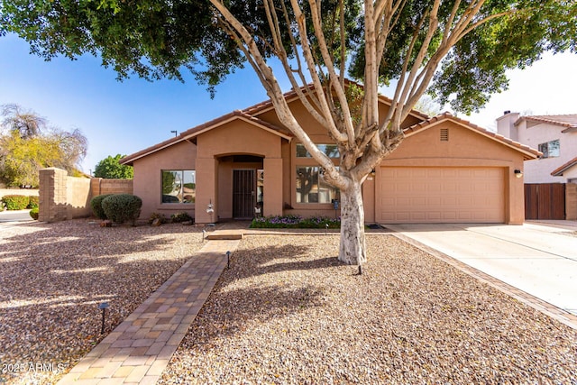 view of front of house with stucco siding, a garage, driveway, and fence