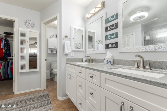 bathroom with double vanity, a spacious closet, toilet, and a sink