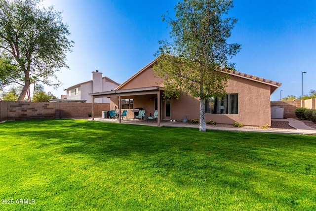 rear view of house with stucco siding, a lawn, a fenced backyard, and a patio area