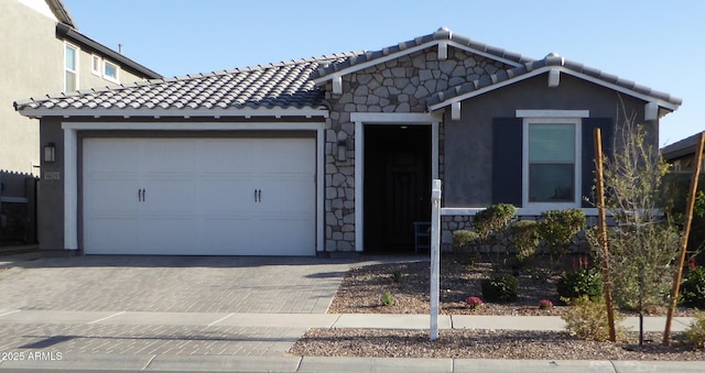 view of front facade featuring a garage, stone siding, a tiled roof, decorative driveway, and stucco siding