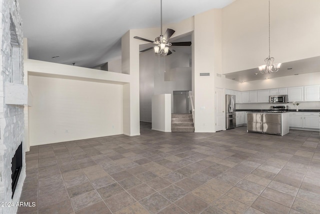 unfurnished living room featuring ceiling fan with notable chandelier, a high ceiling, and a stone fireplace