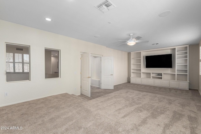 unfurnished living room featuring ceiling fan, built in shelves, and light colored carpet