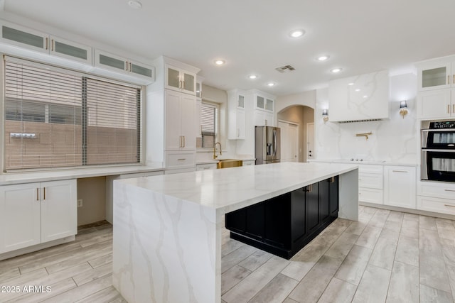 kitchen with visible vents, a center island, wood finish floors, arched walkways, and stainless steel appliances