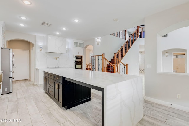 kitchen with visible vents, arched walkways, appliances with stainless steel finishes, white cabinets, and dark cabinets