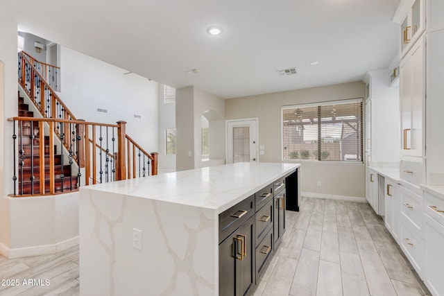 kitchen with white cabinetry, glass insert cabinets, visible vents, and a kitchen island