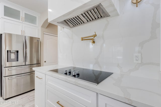 kitchen with ventilation hood, glass insert cabinets, stainless steel fridge, white cabinetry, and black electric cooktop