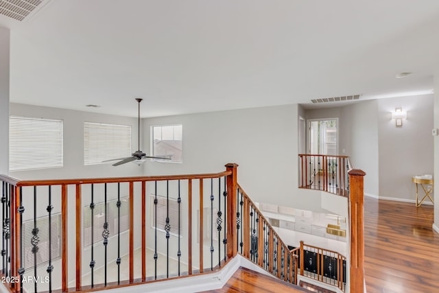 hall with an upstairs landing, visible vents, baseboards, and wood finished floors