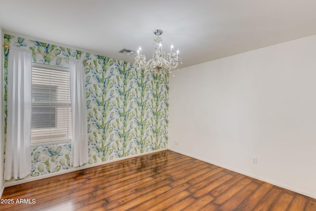 spare room with visible vents, baseboards, an inviting chandelier, and wood finished floors