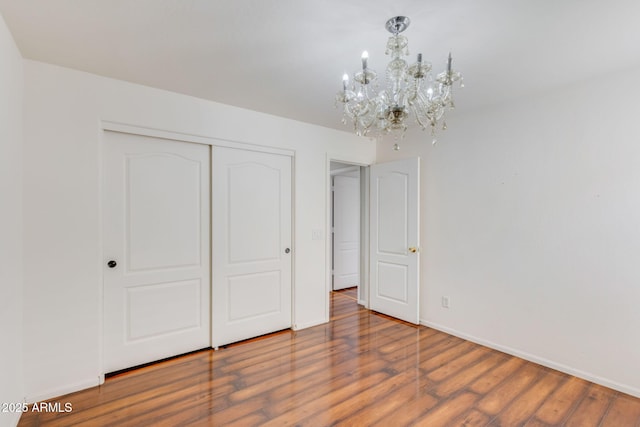 unfurnished bedroom featuring a chandelier, baseboards, a closet, and wood finished floors